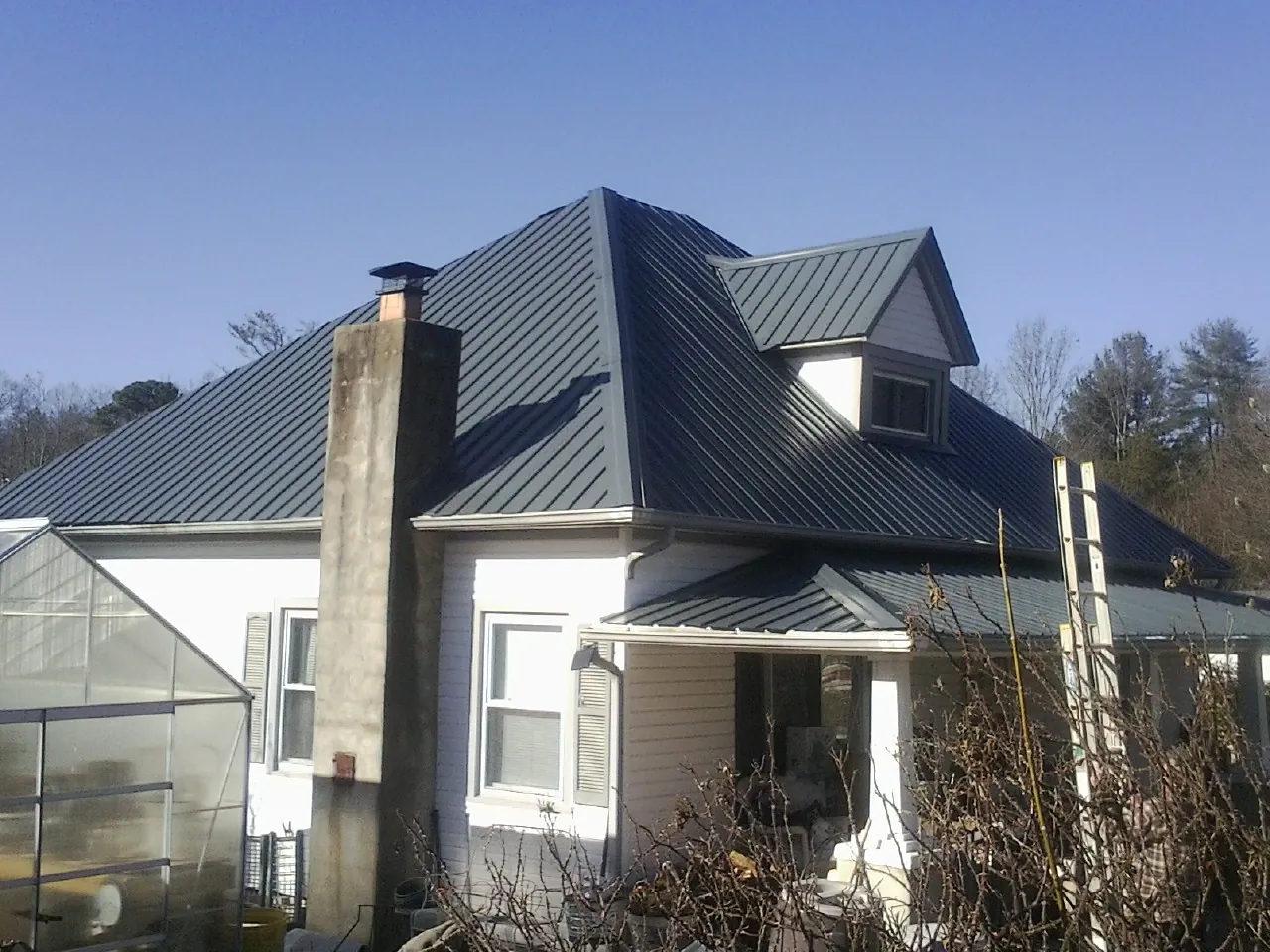 Dark blue standing seam metal roof on a white farmhouse with dormer — Slate & Tile Roof Repair by Roofing Brothers in Ilion