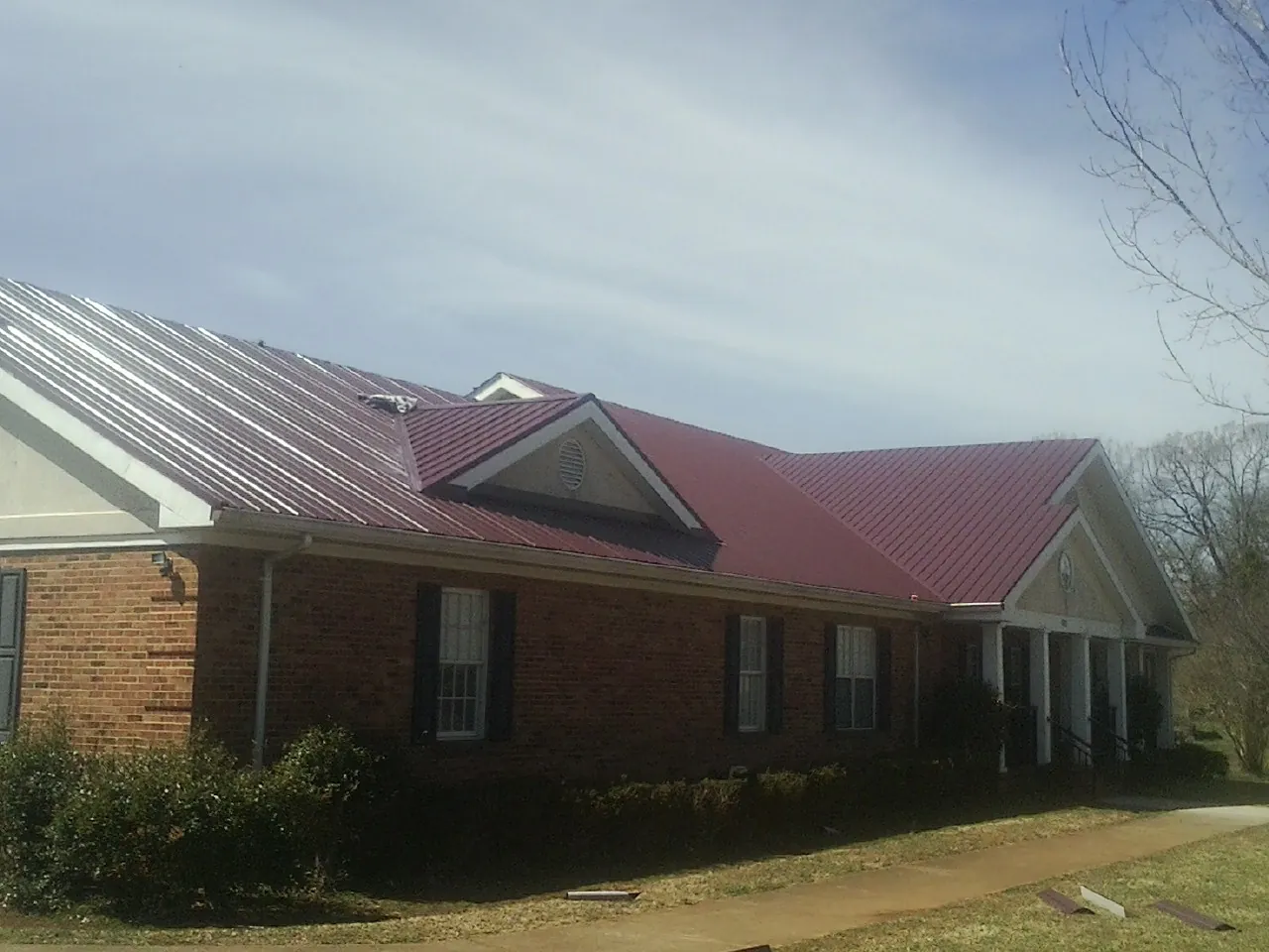 Red metal roof with gabled entries on a long brick building, from a Hail Damage Roof Repair job in Ilion