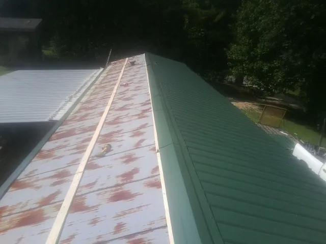 Old rusted panels beside newly installed green metal roofing — Wind Damage Roof Repair by Roofing Brothers in Ilion