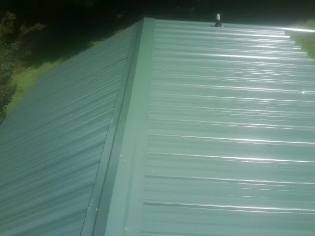 New green metal panels meeting at the ridge of a roof — Flat Roof Repair work by our crew in Ilion