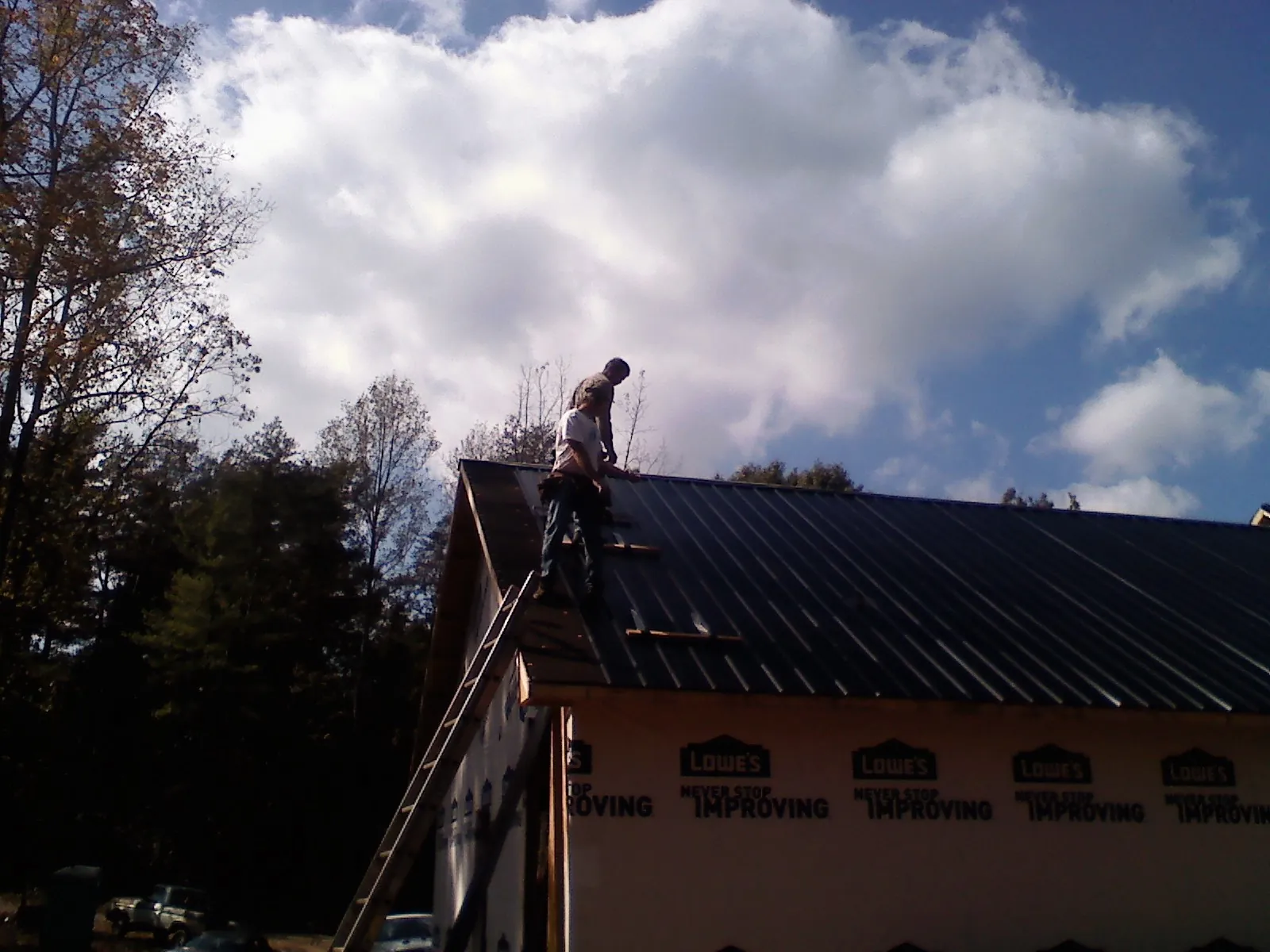 Roofer fastening dark metal panels high against a cloudy sky, from a Roof Inspection job in Ilion