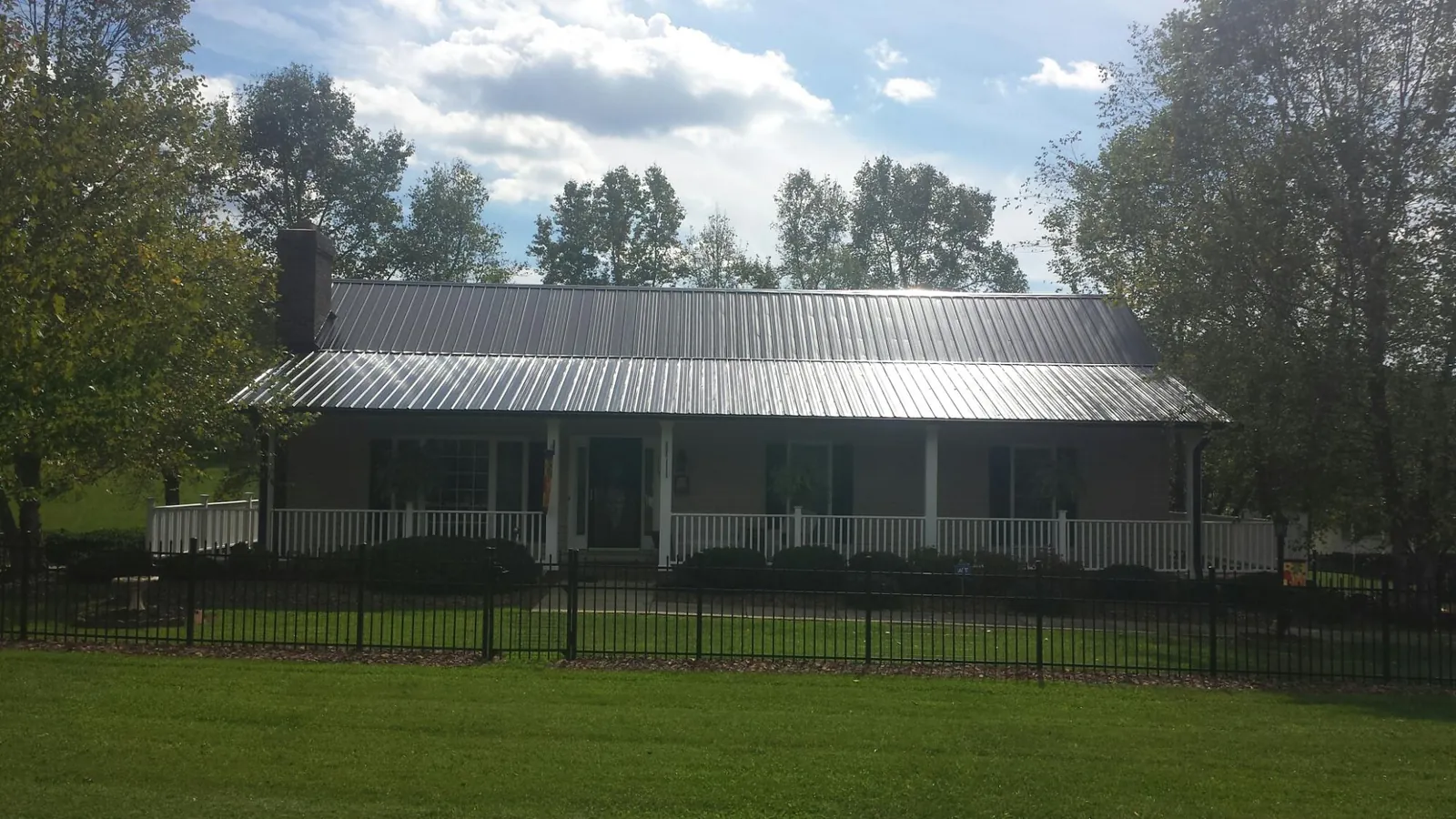 Gray metal roof on a brick ranch with a full width front porch — Gutter Guard Installation work by our crew in Ilion